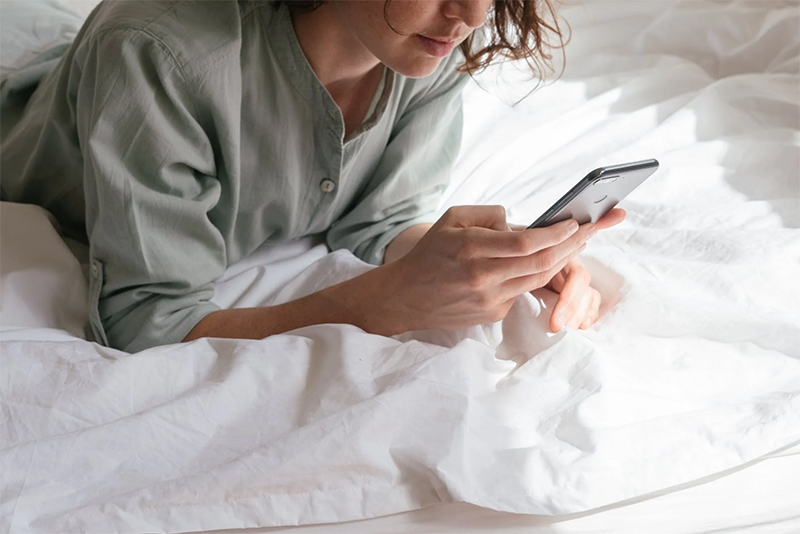 Mulher deitada na cama usando smartphone